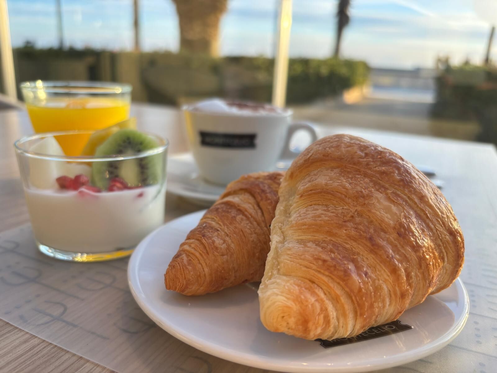 Une table dressée pour le petit-déjeuner, avec des croissants, un verre de jus d’orange et une tasse de café, le tout placé de manière à profiter de la vue.