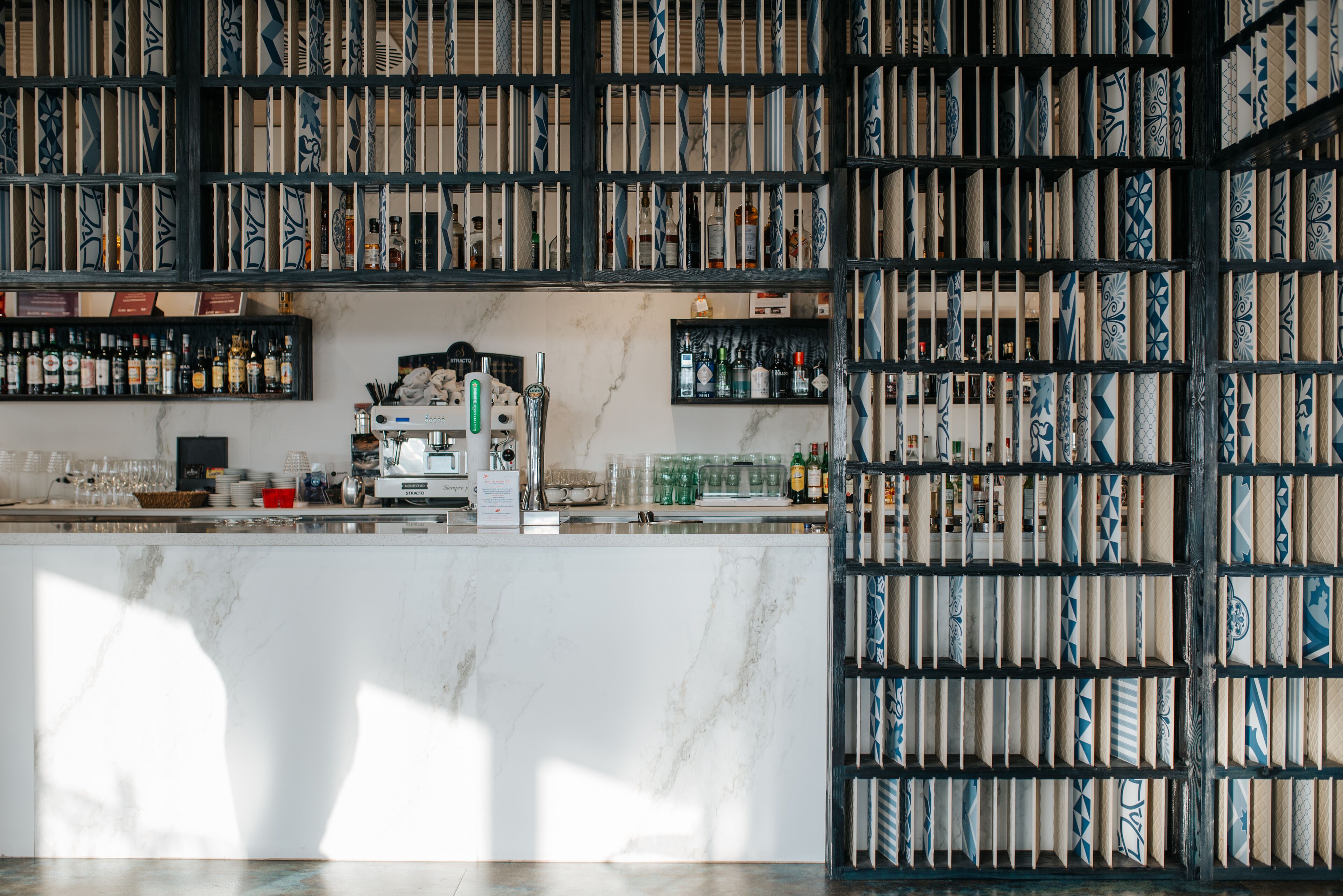 A bar area with shelves of bottles and glasses, a marble counter, and a patterned wall.
