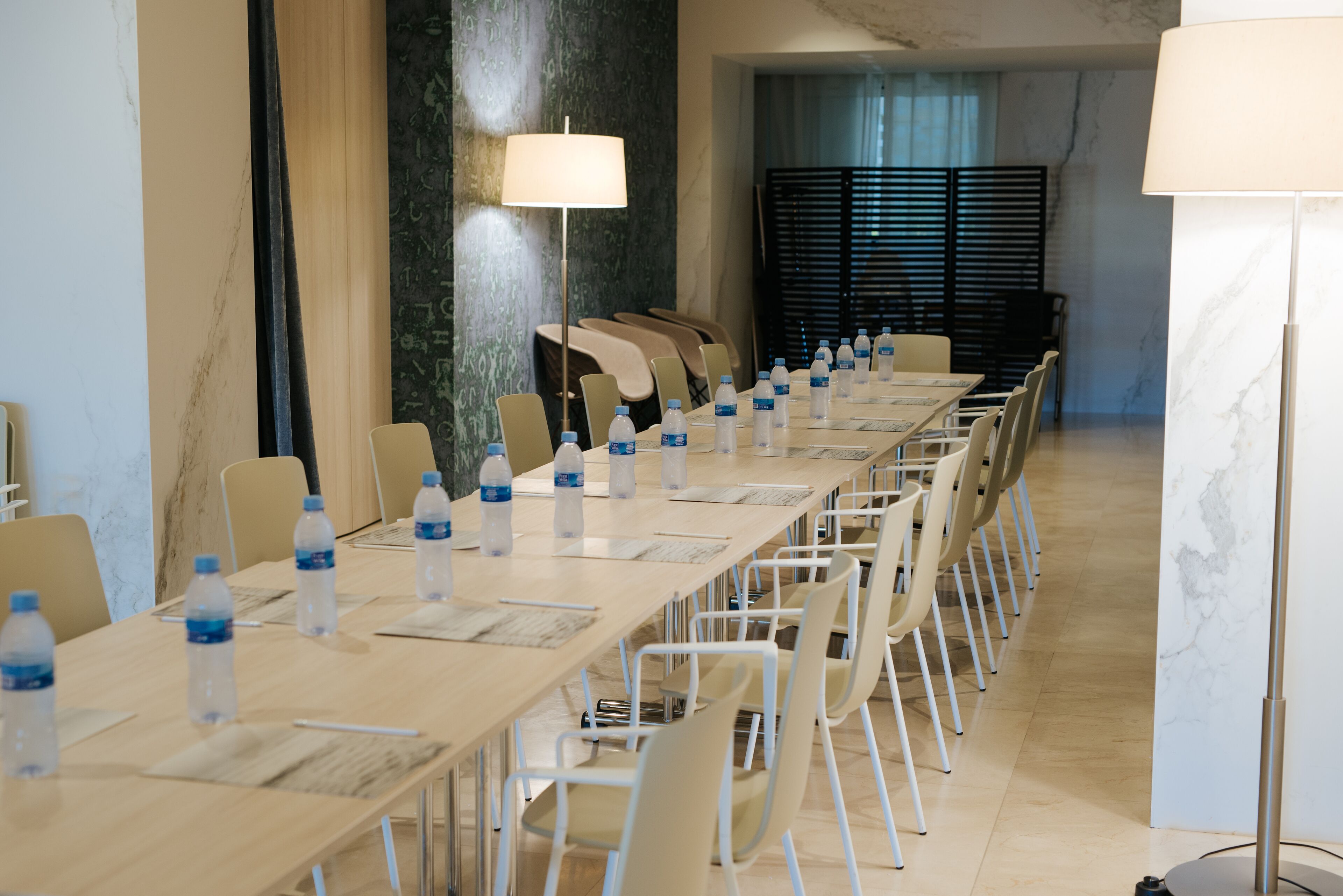 Un salón de conferencias con una larga mesa, sillas, botellas de agua y una lámpara.