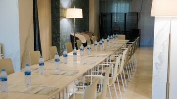 Un salón de conferencias con una larga mesa, sillas, botellas de agua y una lámpara.