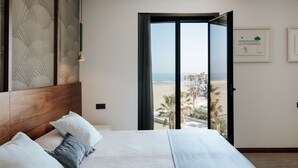 Ein Schlafzimmer mit einem großen Bett, einem Holzkopfende, Blick auf den Strand und einem gerahmten Bild an der Wand.