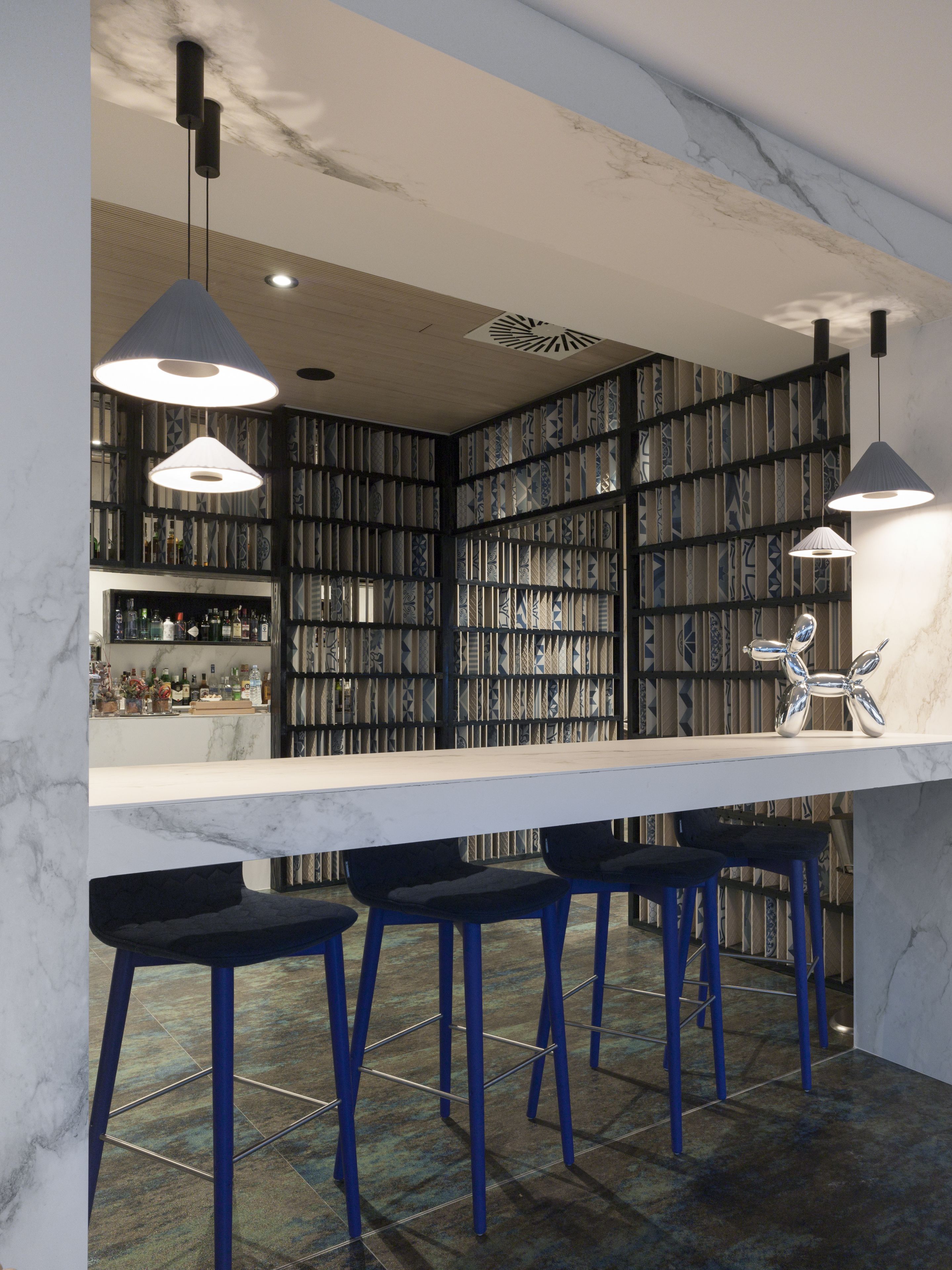 Zona de bar moderna con encimera de mármol, taburetes azules y lámparas colgantes.
