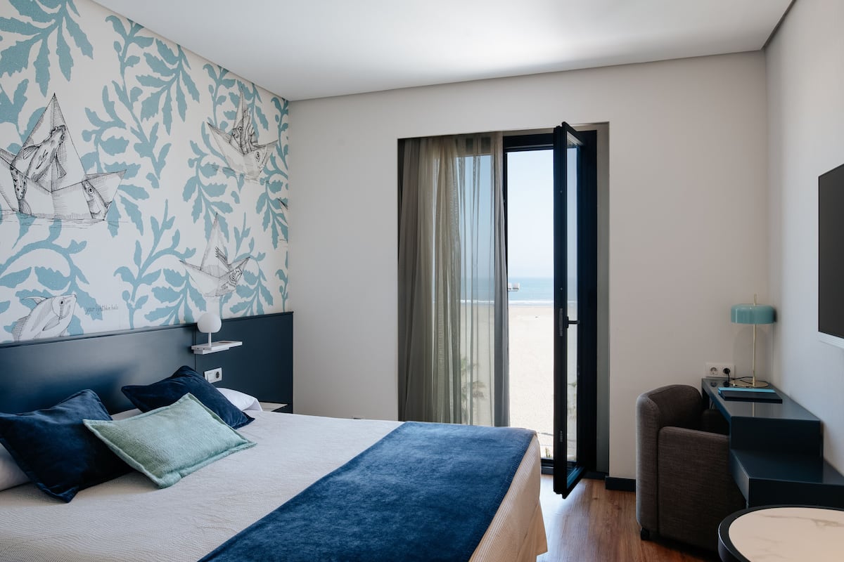 Habitación de hotel con cama, escritorio, silla y vistas a la playa, además de un balcón.