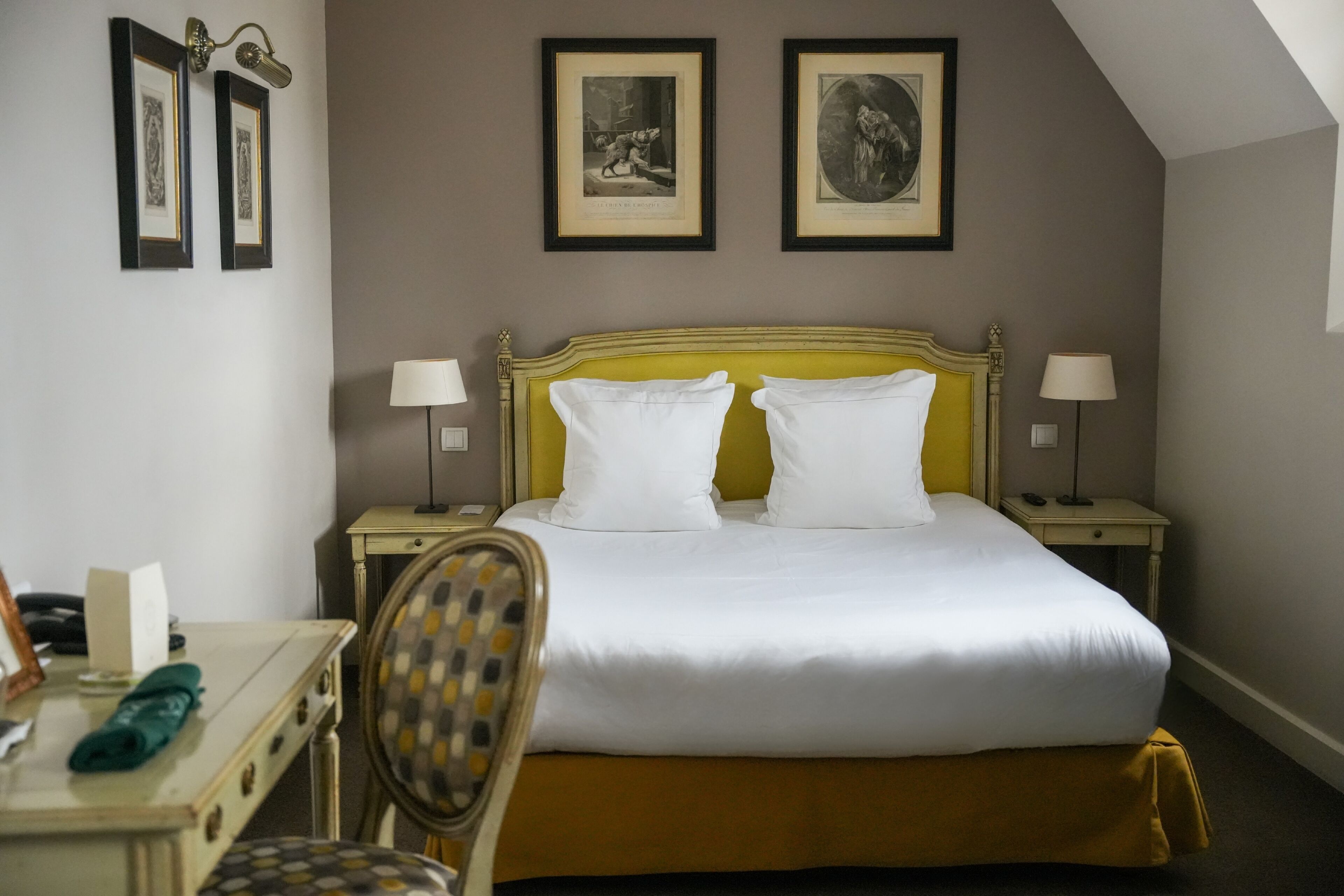 Een hotelkamer met een bed, twee nachtkastjes, een stoel en ingelijste foto's aan de muur.