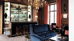 A bar area with shelves of bottles and glasses, a blue sofa, and a chandelier. - Château Sainte Sabine (Sainte-Sabine)