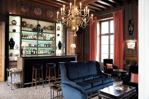 A bar area with shelves of bottles and glasses, a blue sofa, and a chandelier. - Château Sainte Sabine (Sainte-Sabine)
