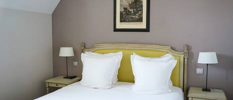 Une chambre d’hôtel avec un lit, deux tables de chevet avec des lampes, un tableau encadré au mur et un plafond en pente.