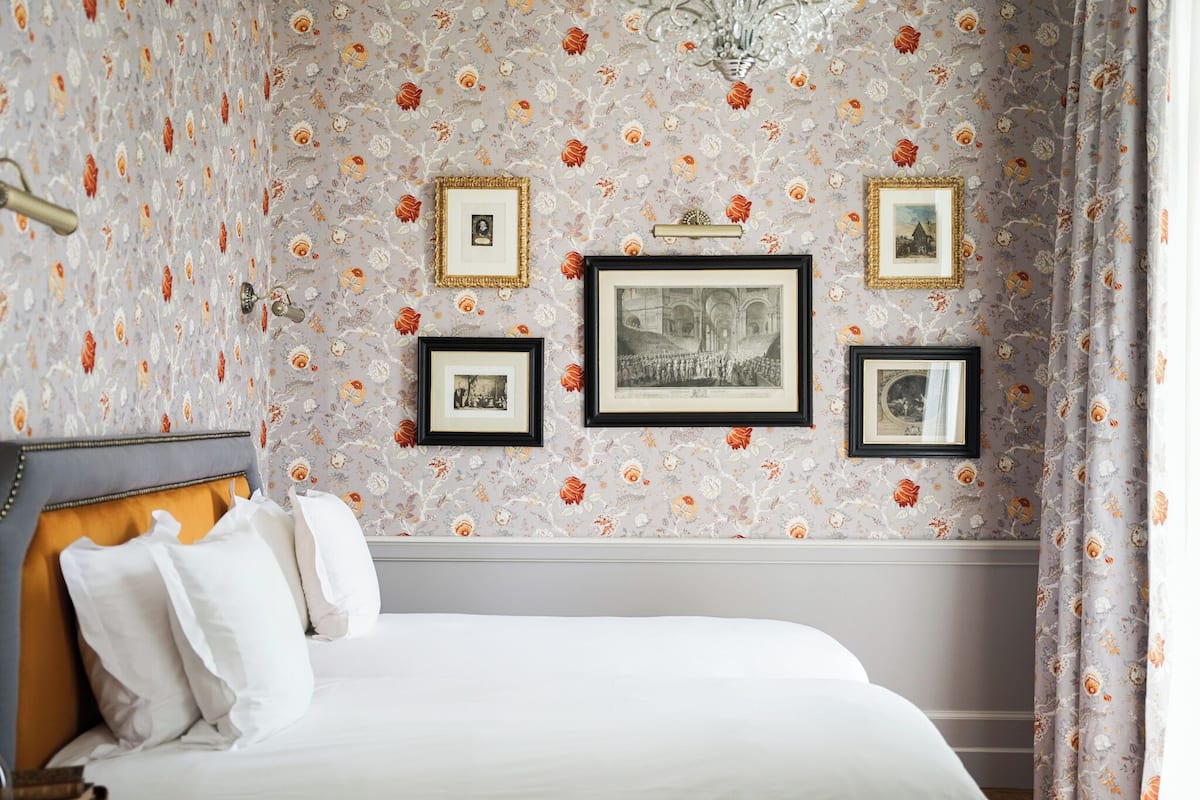 Ein Hotelzimmer mit floralem Wandpapier, einem Bett mit weißer Bettwäsche und gerahmten Bildern an der Wand.