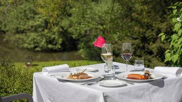 An outdoor dining table with plates of food, glasses of wine, and a pink flower.