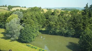 Une vue sur la rivière, avec une zone herbeuse et des arbres, une étendue d'eau calme, et une rangée de chaises le long du bord de l'eau.