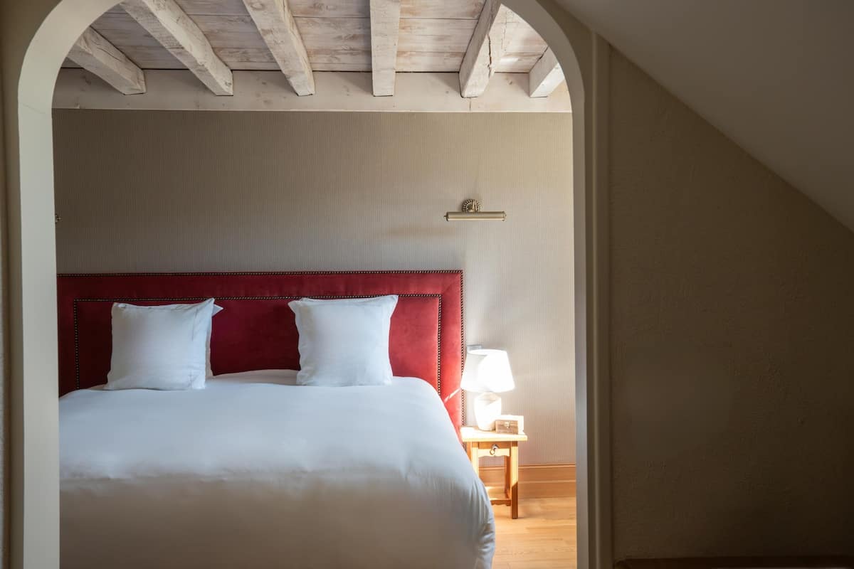 Ein Schlafzimmer mit rotem, gepolstertem Kopfteil, weißer Bettwäsche, einem Nachttisch mit Lampe und Holzboden.