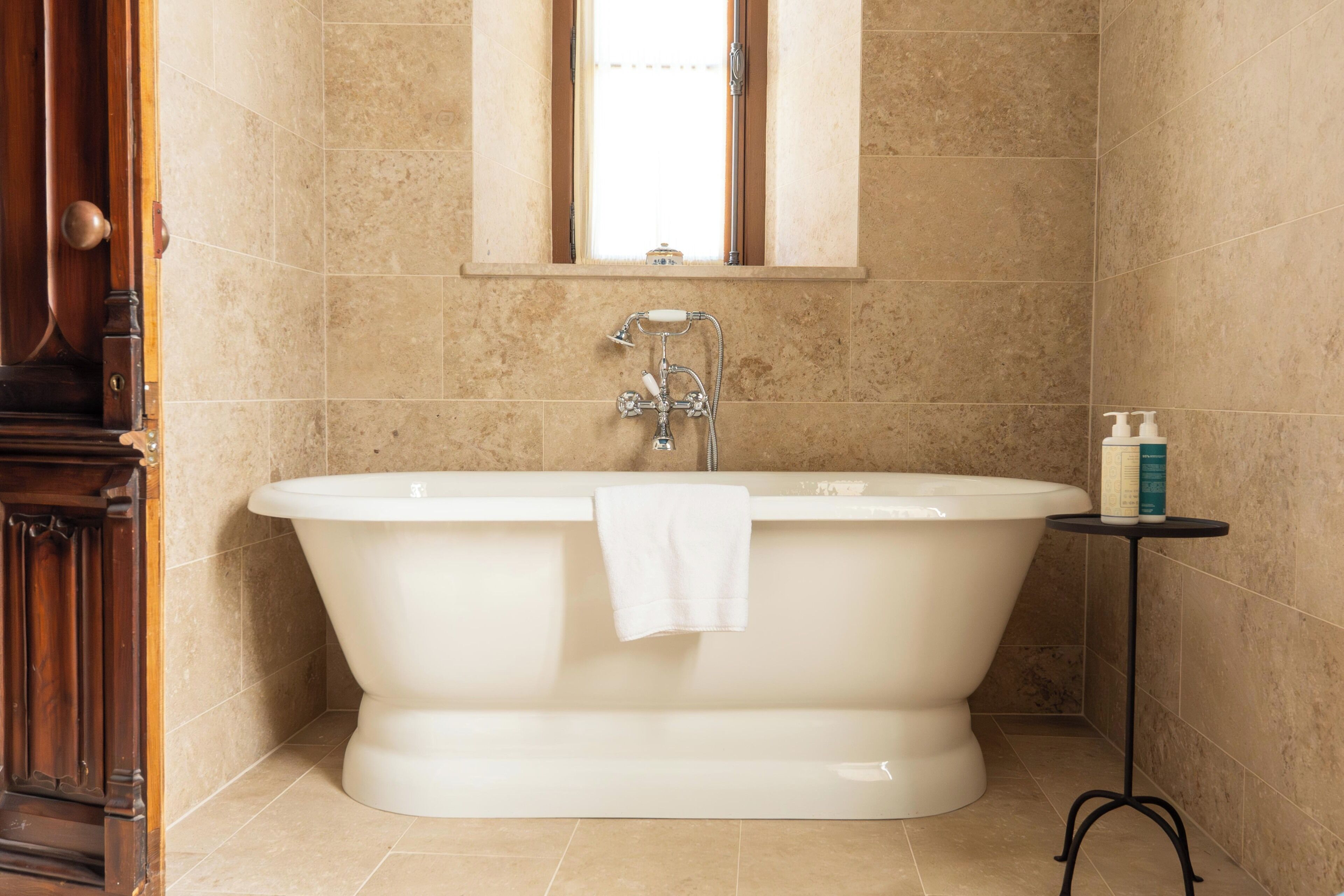 Ein Badezimmer mit einer freistehenden Badewanne, einem Fenster darüber und einem kleinen Tisch mit Toiletteartikeln.