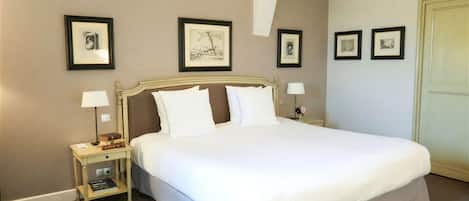 Una cama bien hecha con sábanas blancas, una mesita de noche con lámpara y cuadros en la pared.