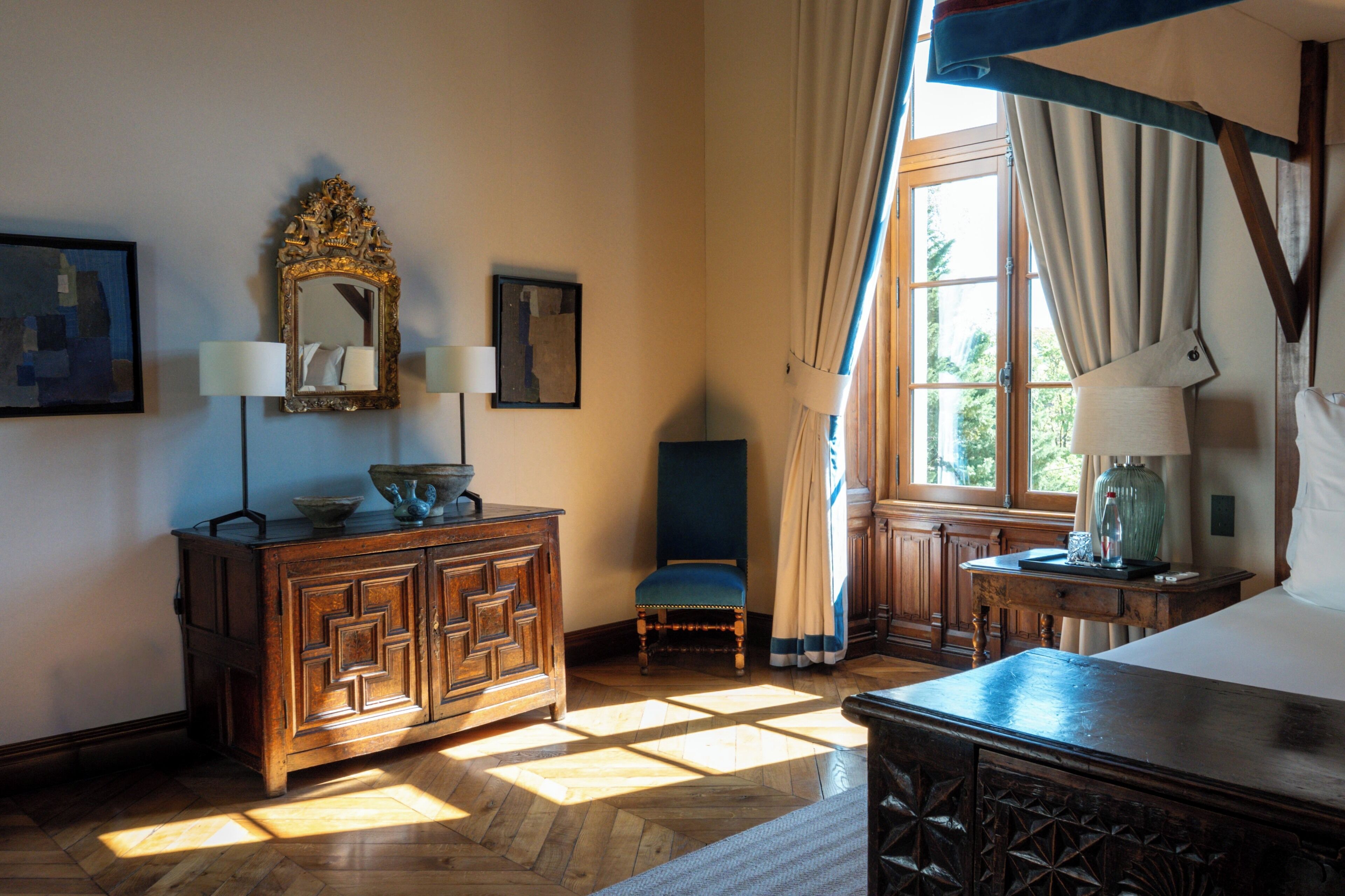 Une pièce comprenant une commode en bois, une chaise, un lit à baldaquin et une fenêtre avec des rideaux.