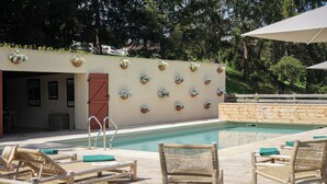 Uma área à beira da piscina com espreguiçadeiras, um deck de madeira e uma parede decorada com vasos de flores.