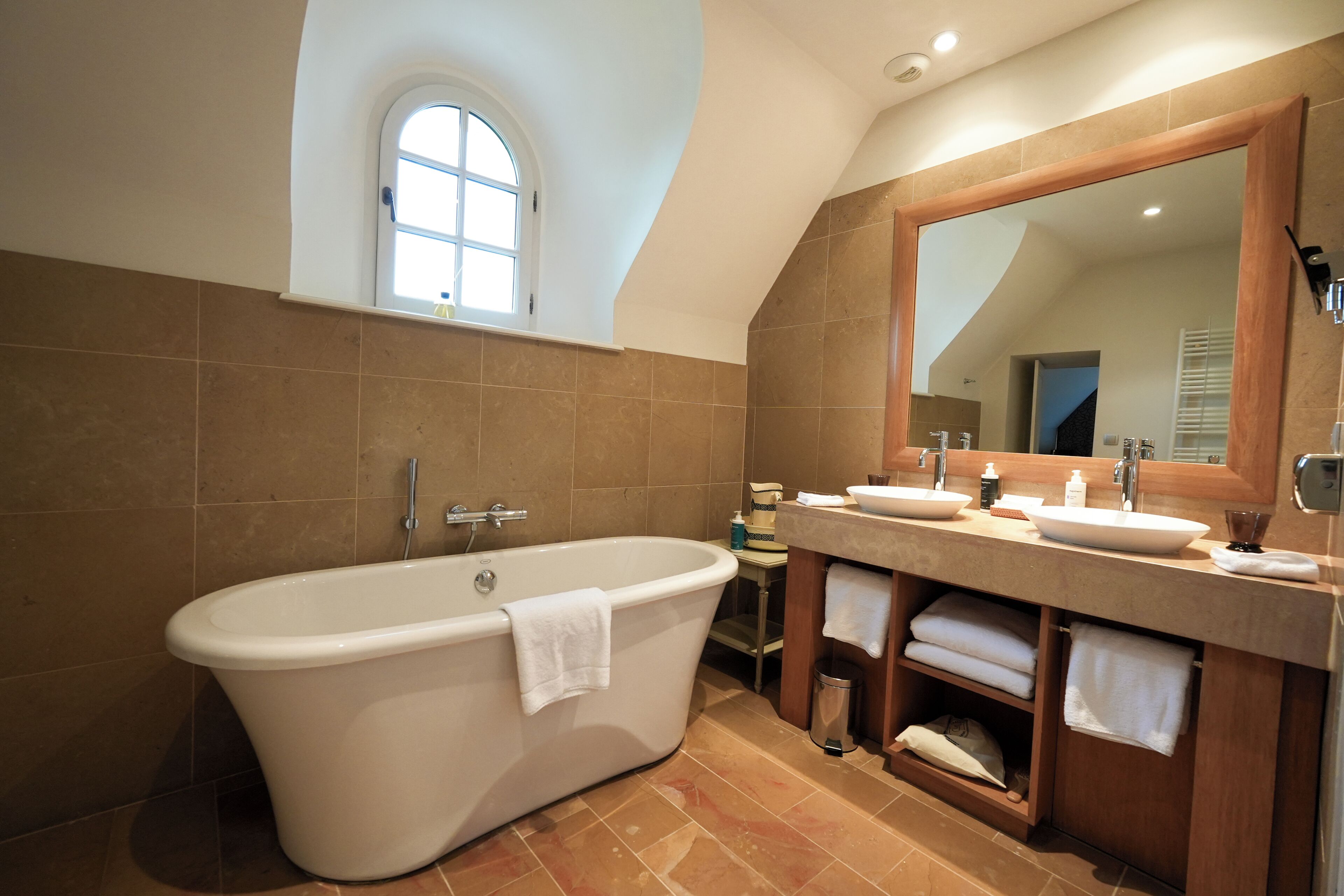 A modern bathroom with a freestanding bathtub, dual sinks, a large mirror, and a window with a view.