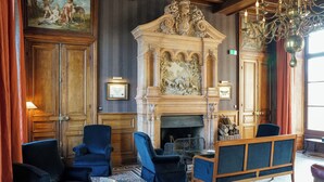 A room with a fireplace, blue upholstered chairs, a wooden bench, and a chandelier. - Château Sainte Sabine (Sainte-Sabine)