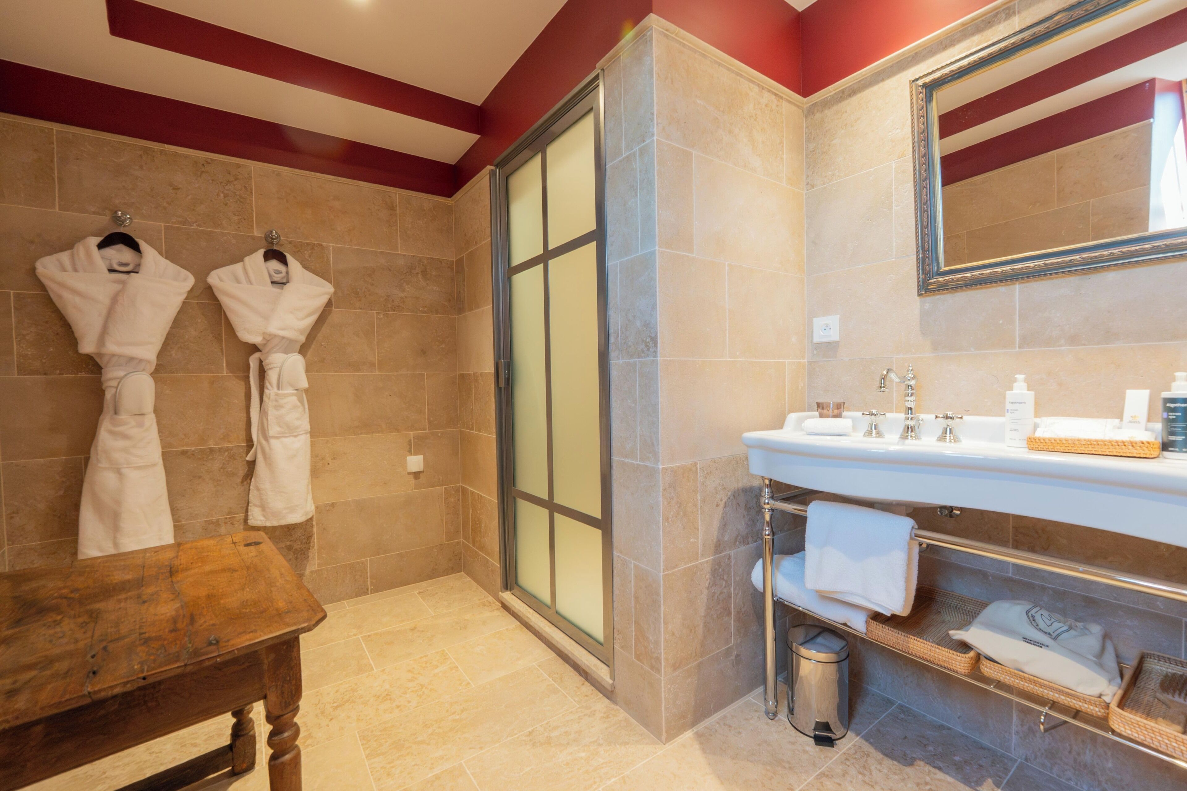 A bathroom with a shower, a sink with toiletries, and two white towels hanging on hooks.