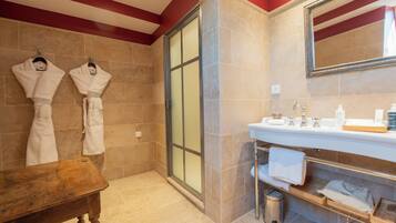A bathroom with a shower, a sink with toiletries, and two white towels hanging on hooks.