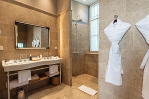 A bathroom with a sink, mirror, shower, and two white robes hanging on the wall. - Château Sainte Sabine (Sainte-Sabine)