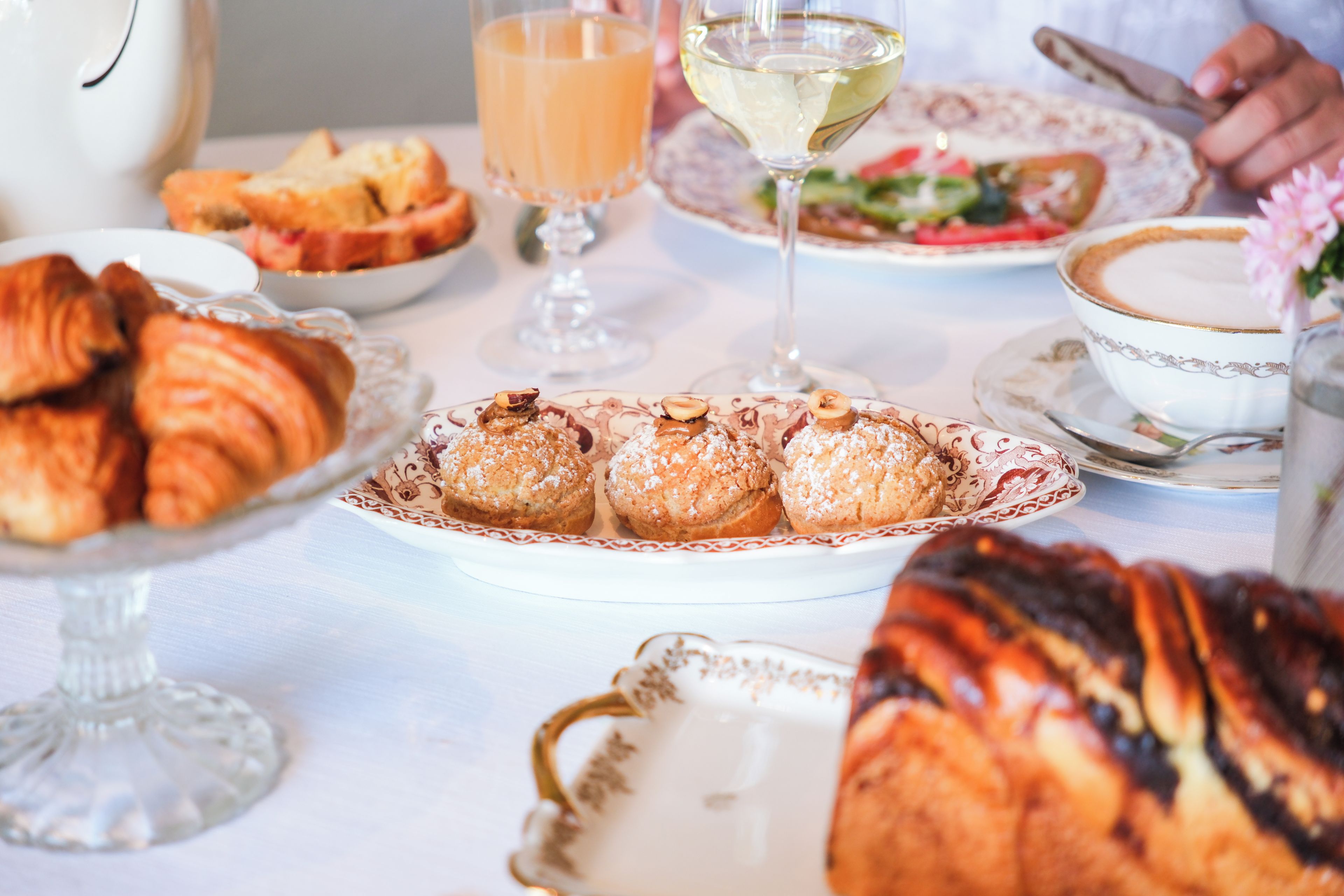 Una mesa servida con diversos pasteles, una copa de vino blanco y una taza de café.