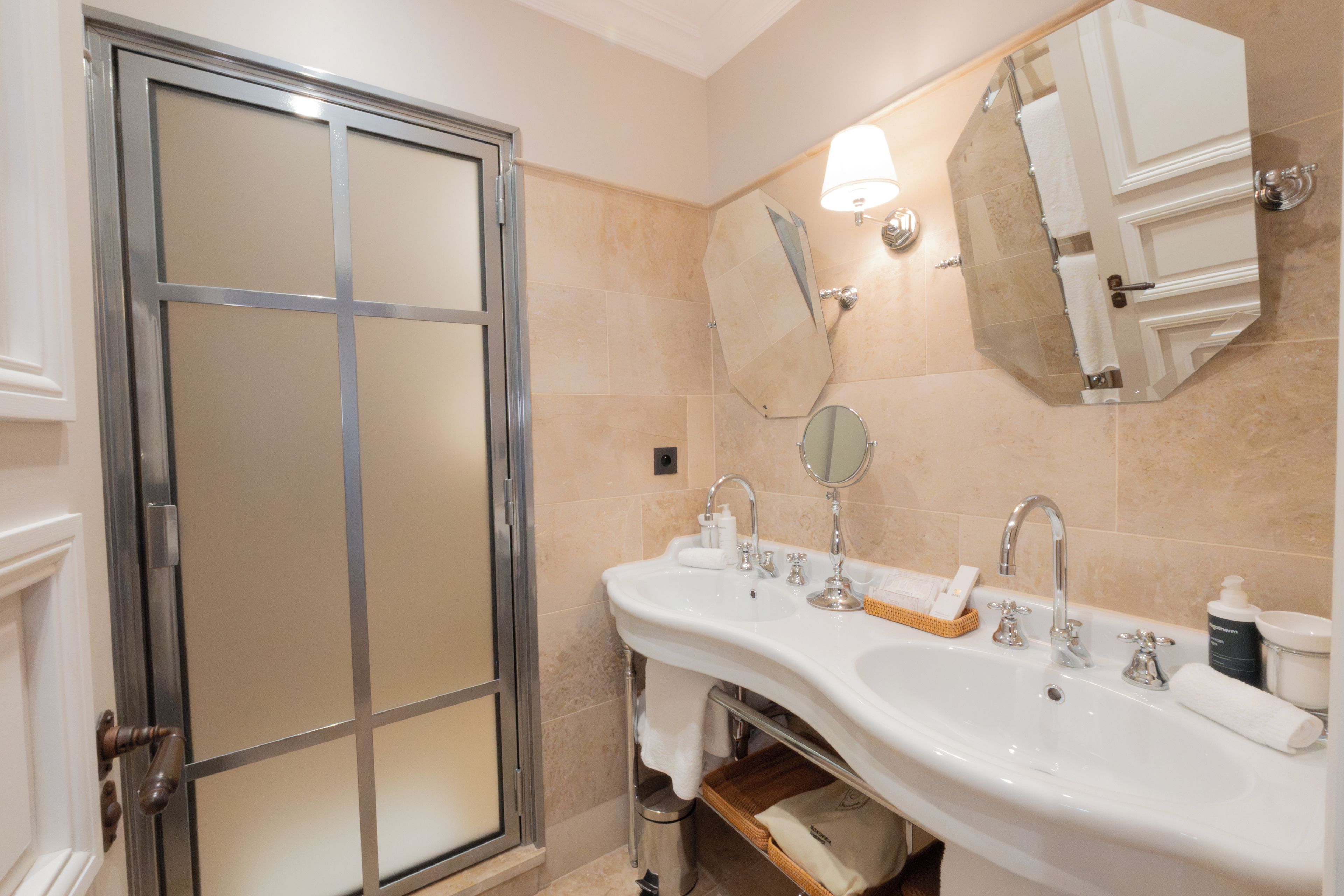 A bathroom with a glass shower door, a double sink with a mirror above, and a towel rack.
