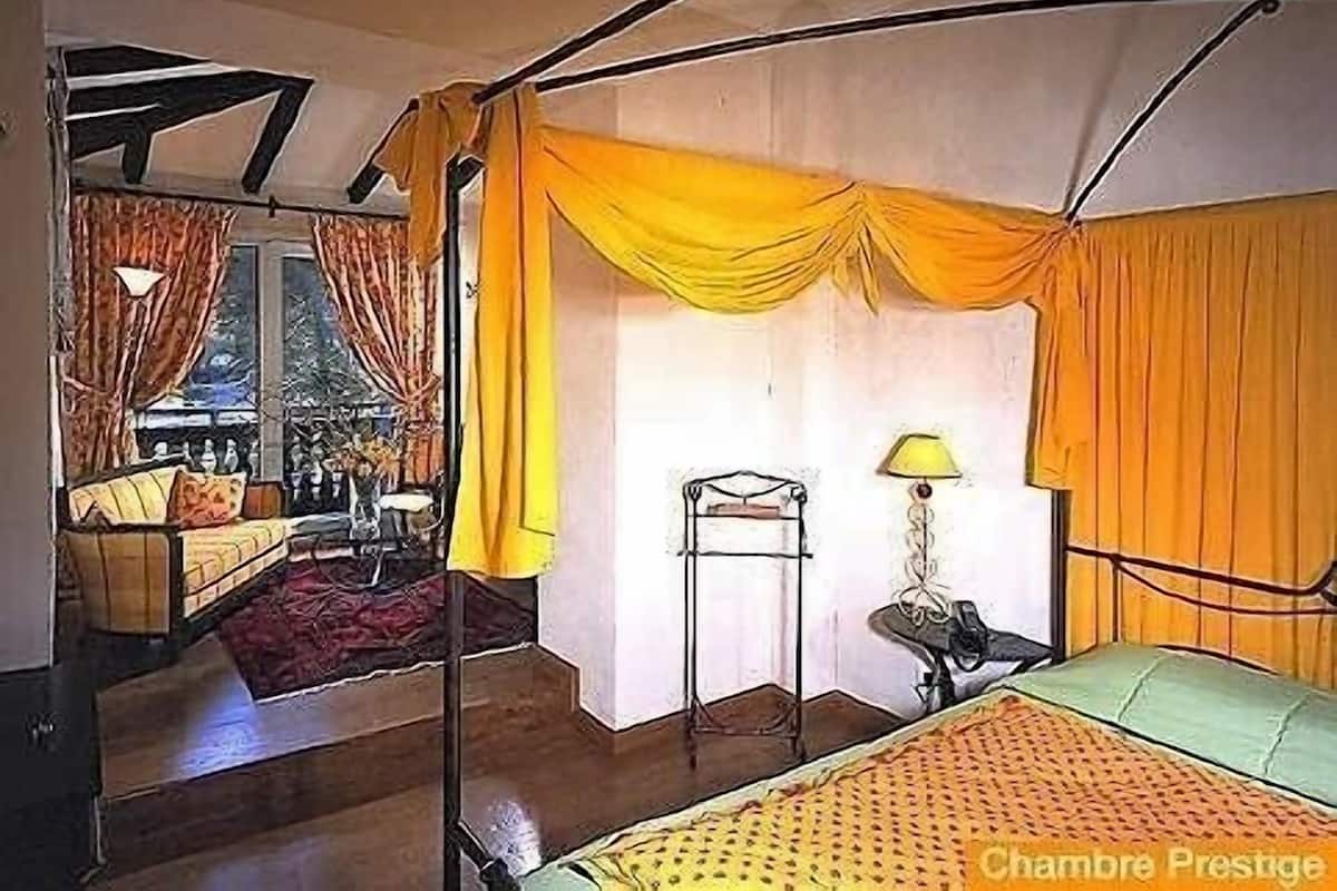 Ein Zimmer mit einem Bett, einem Sessel, einem Tisch und einem Fenster mit Vorhängen.