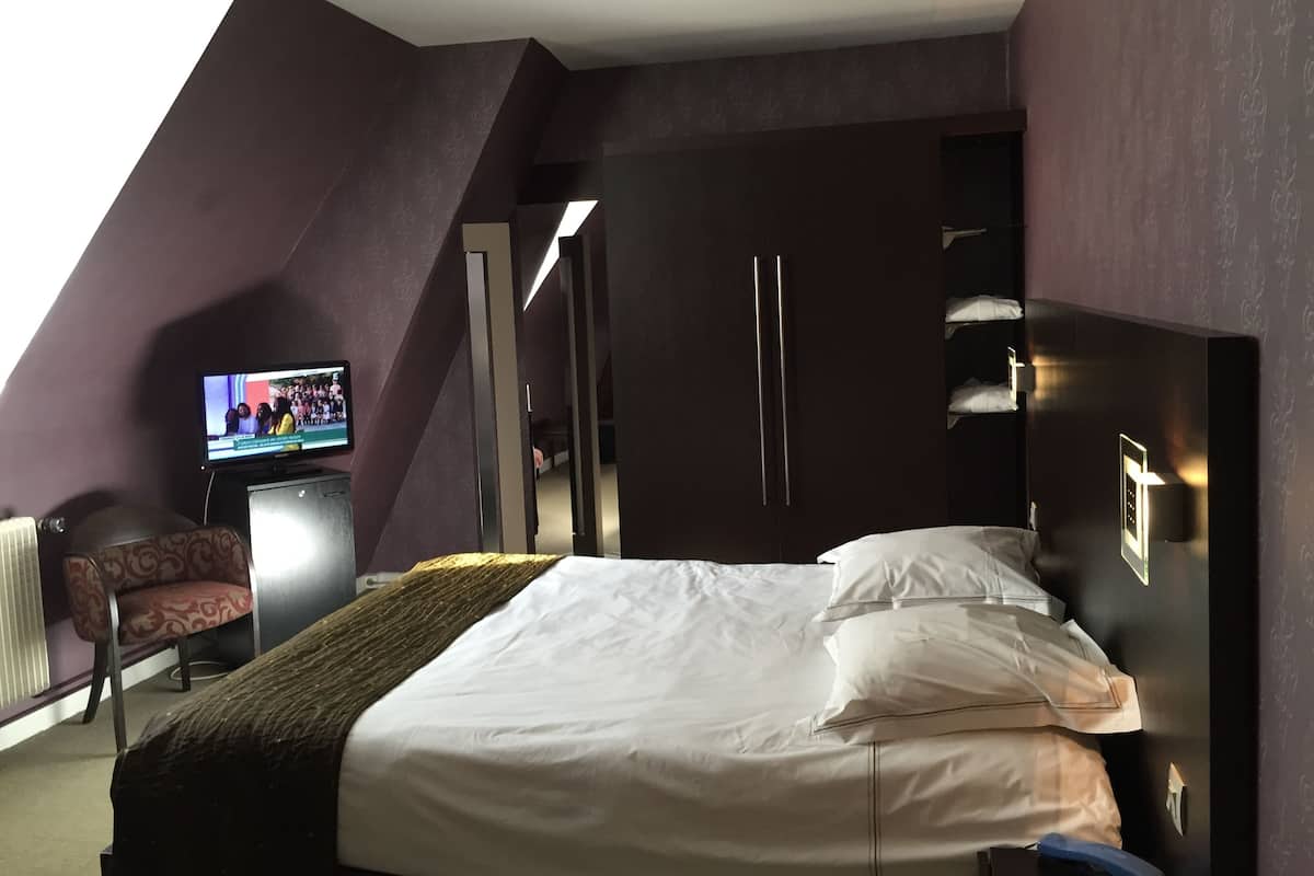 Ein modernes Hotelzimmer mit einem großen Bett, einem Fernseher, einem Kleiderschrank und einer Sitzecke mit einem Sessel.