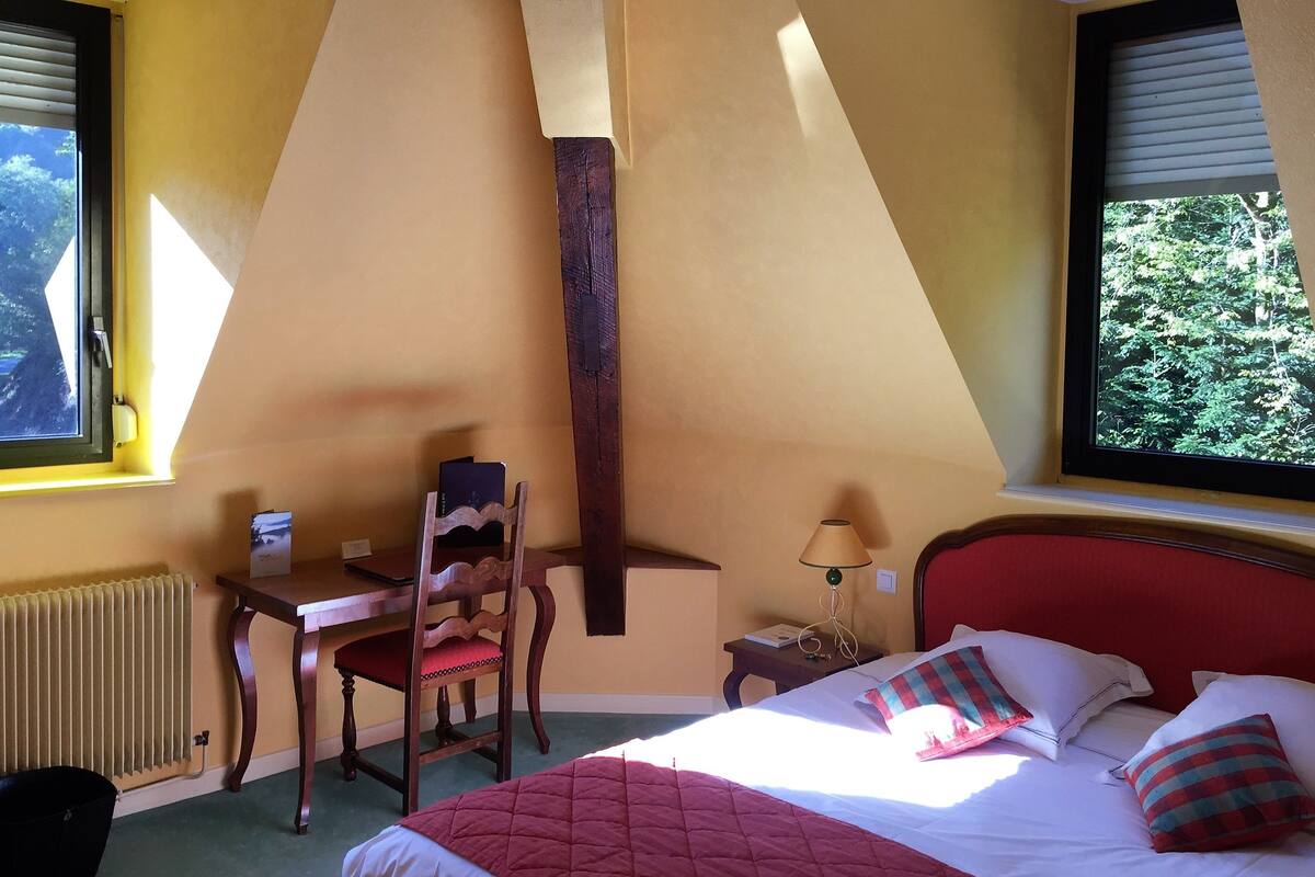 Ein Schlafzimmer mit Bett, Stuhl, Schreibtisch und Fenster mit Blick auf Bäume.