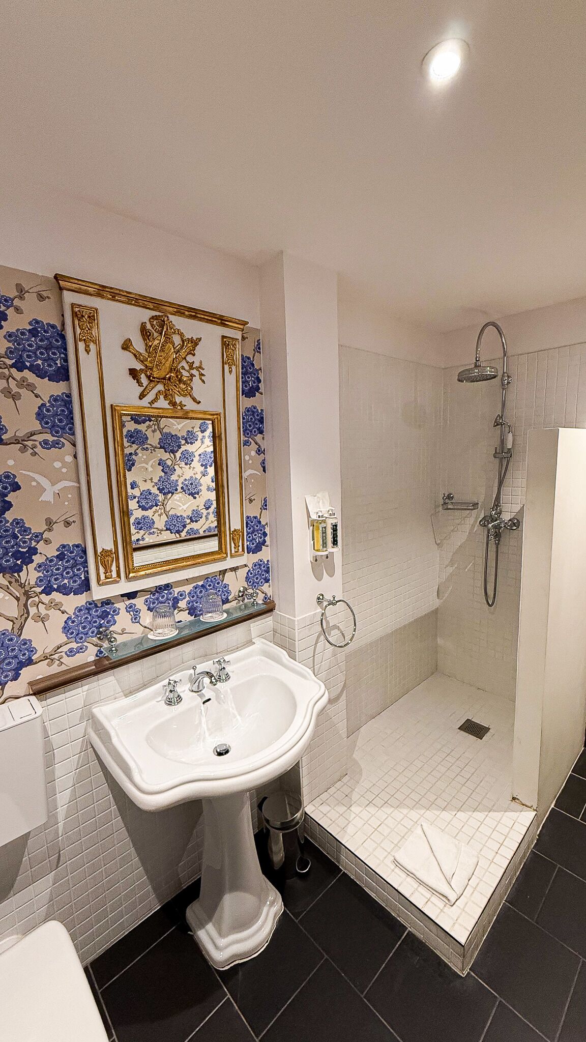 Casa de banho com lavatório branco, cabine de duche em vidro e parede decorativa com motivos florais.