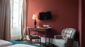 A hotel room with a bed, a desk with a lamp, a chair, a television, and a window with curtains.