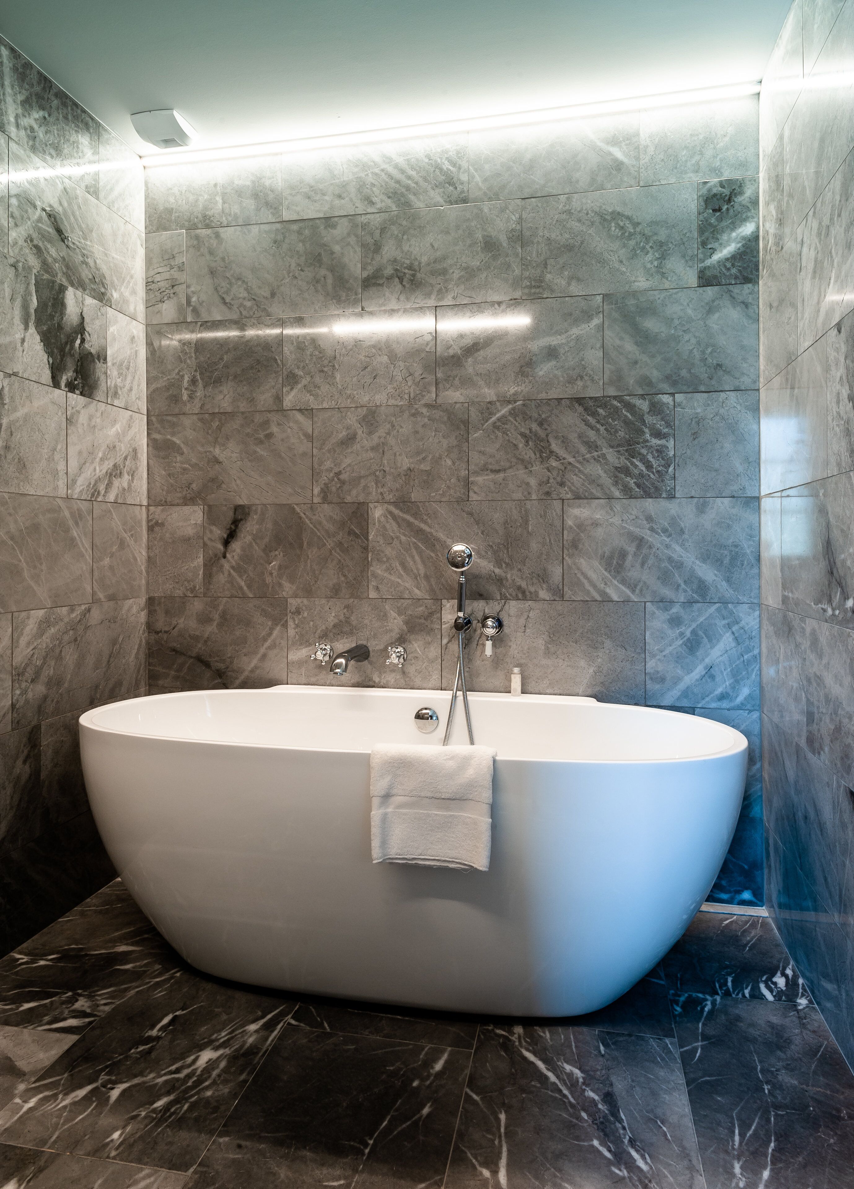 A modern bathroom with a freestanding bathtub, marble walls, and a built-in showerhead.