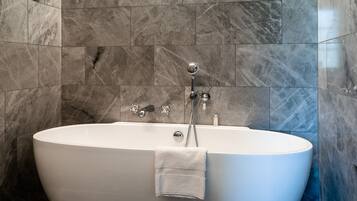 A modern bathroom with a freestanding bathtub, marble walls, and a built-in showerhead.