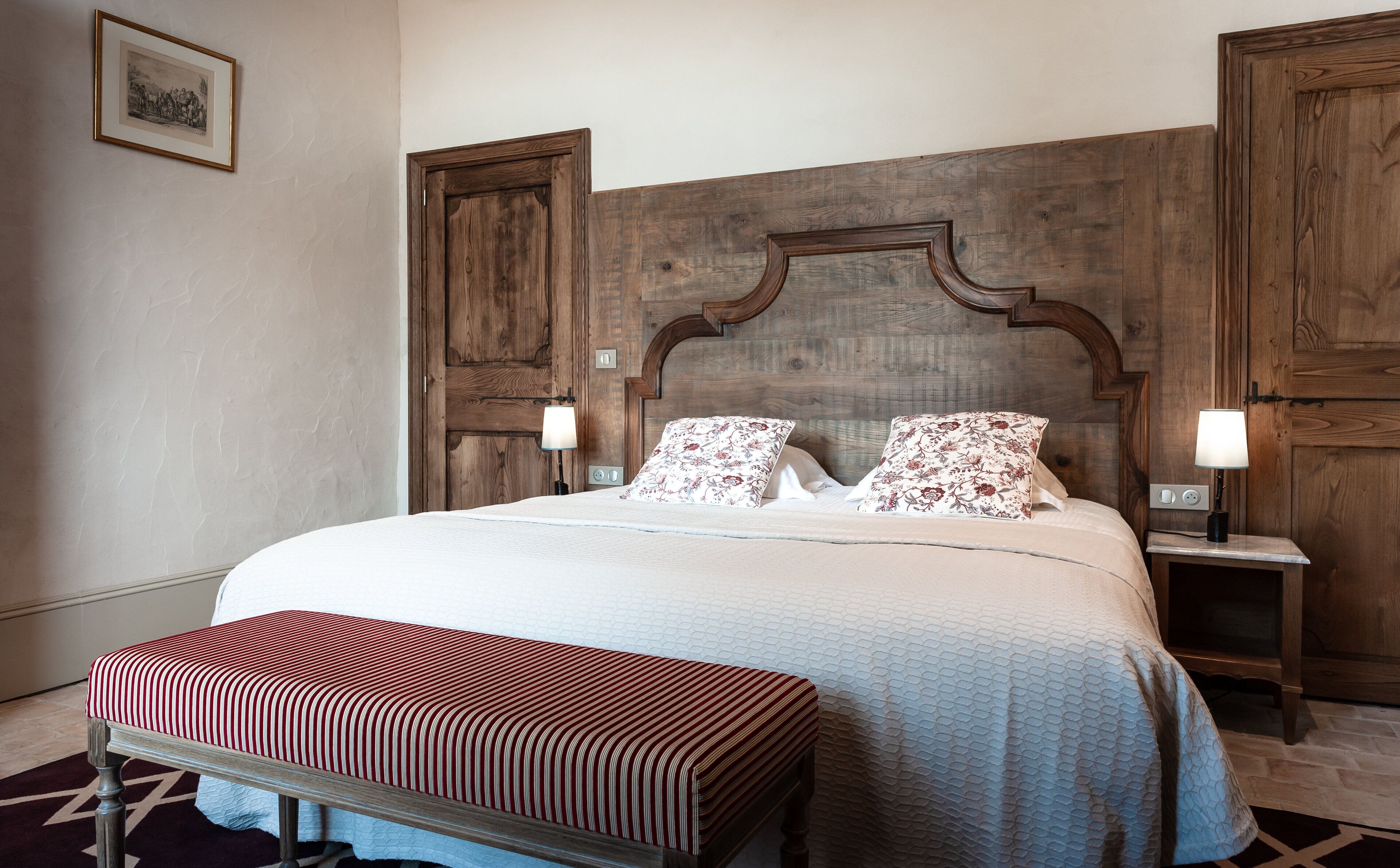 A neatly made bed with floral pillows, a wooden headboard, and a bench at the foot of the bed.