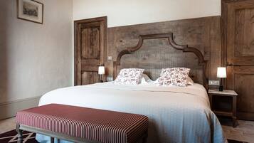 A neatly made bed with floral pillows, a wooden headboard, and a bench at the foot of the bed.