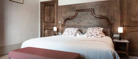 Un lit bien fait, agrémenté de coussins à motifs floraux, d’une tête de lit en bois et d’un banc placé au pied du lit.
