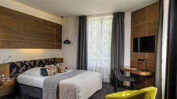 A modern hotel room with a large bed, a desk, a chair, and a TV.