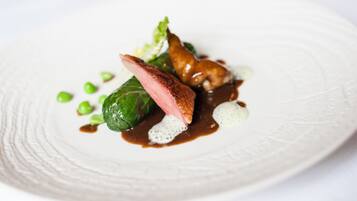 A white plate with a piece of meat, green peas, and a leafy vegetable.
