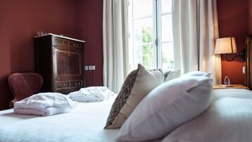 A hotel room with a bed, pillows, a dresser, and a window with curtains.