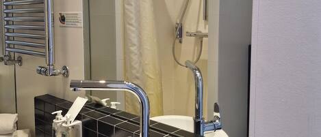 Een badkamer met een wit wastafel, wandtegels in het zwart, een chromen handdoekhouder en een douche met glazen deur.