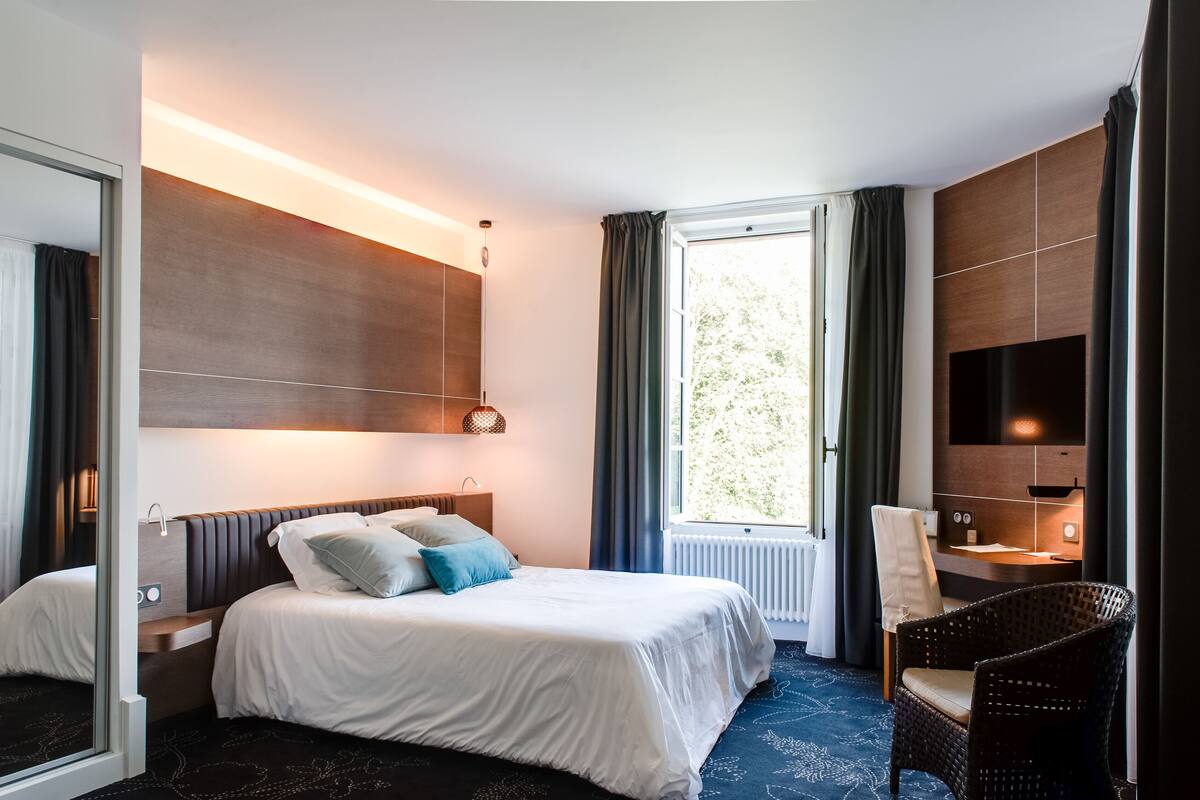A hotel room with a bed, a chair, a desk, a TV, and a window with curtains.