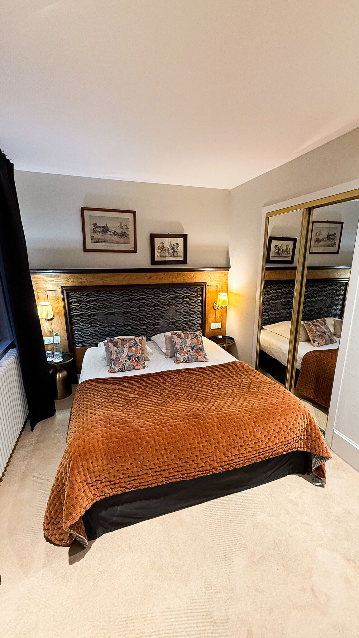 Une chambre d’hôtel avec un grand lit, deux tables de chevet, un miroir et des tableaux encadrés au mur.