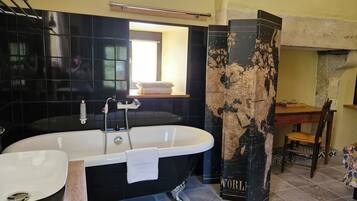 Une salle de bain avec une baignoire noire, un lavabo blanc et une chaise en bois.