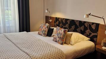 Et hotelværelse med en stor seng, en sengegavl med blomstermønster, to sengeborde med lamper og et vindue med gardiner.