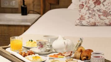 A breakfast tray with eggs, bacon, toast, and pastries on a bed in a hotel room.