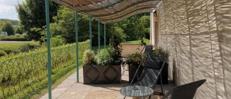 Un patio al aire libre con una zona de estar cubierta, suelo de piedra y plantas en macetas.