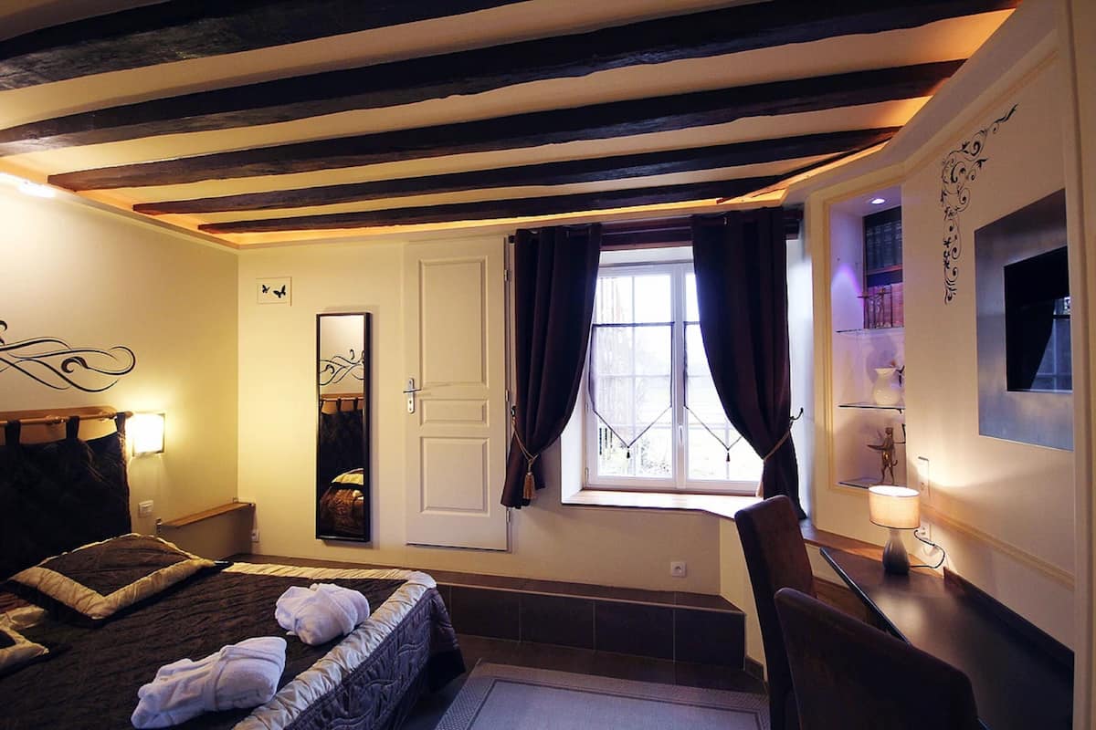 Habitación de hotel con cama, espejo, ventana con cortinas, escritorio con lámpara y una decoración en la pared.