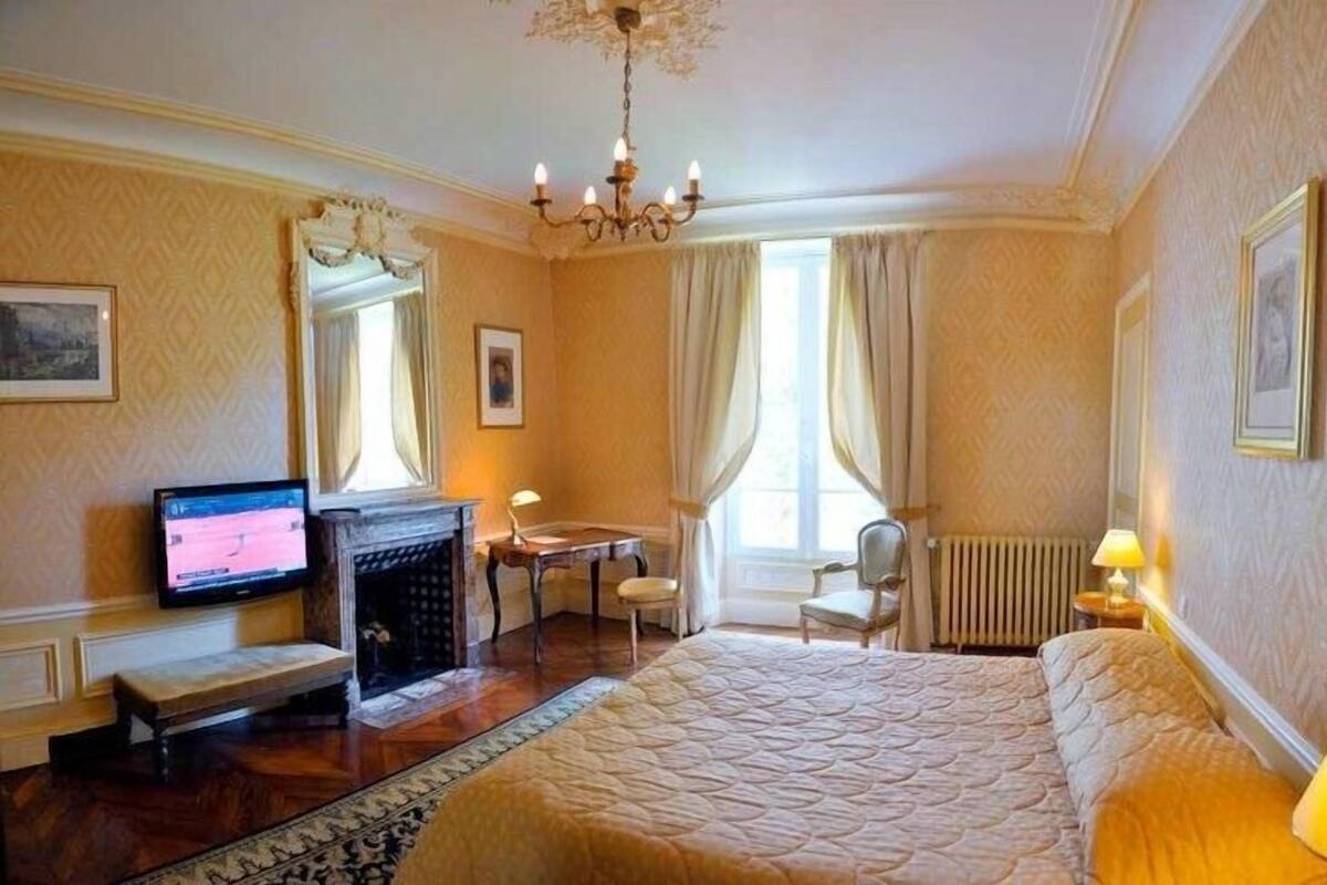 Una habitación de hotel con cama, escritorio, silla, televisor y candelabro.