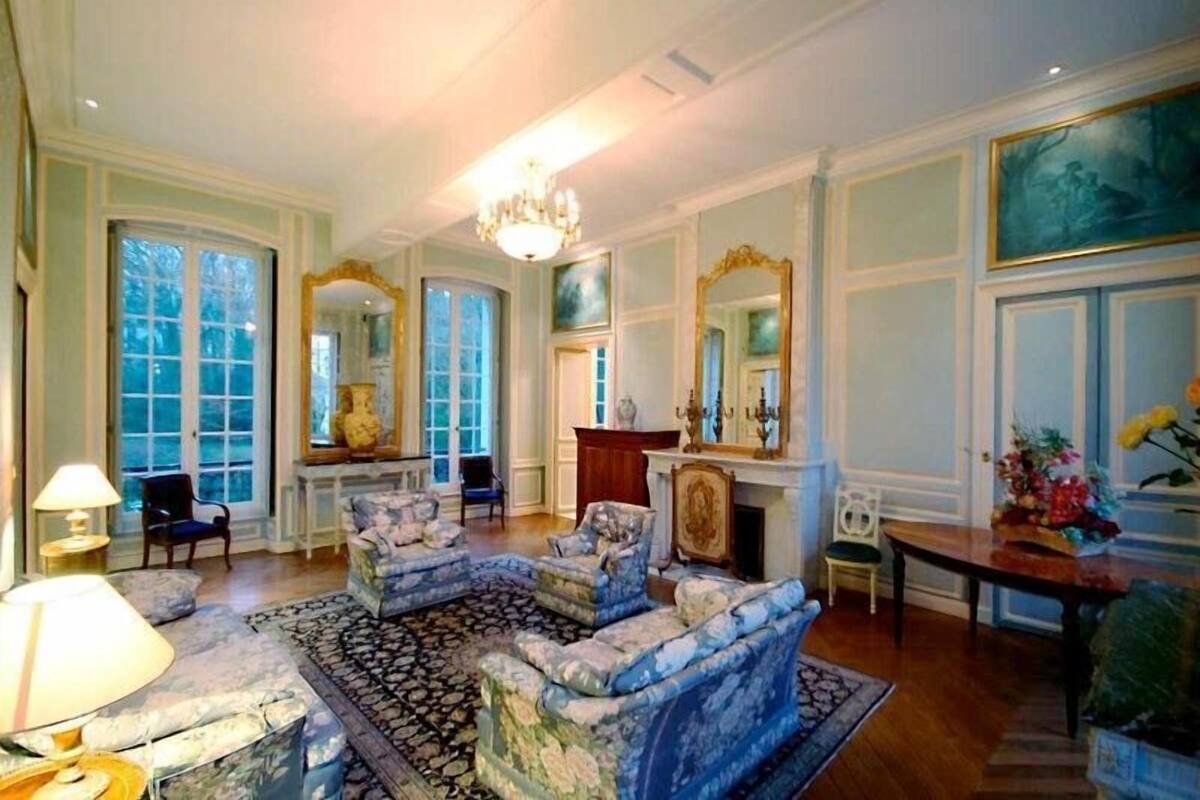 Un salón amplio con una chimenea grande y decorativa, varias zonas de estar y ventanas grandes.