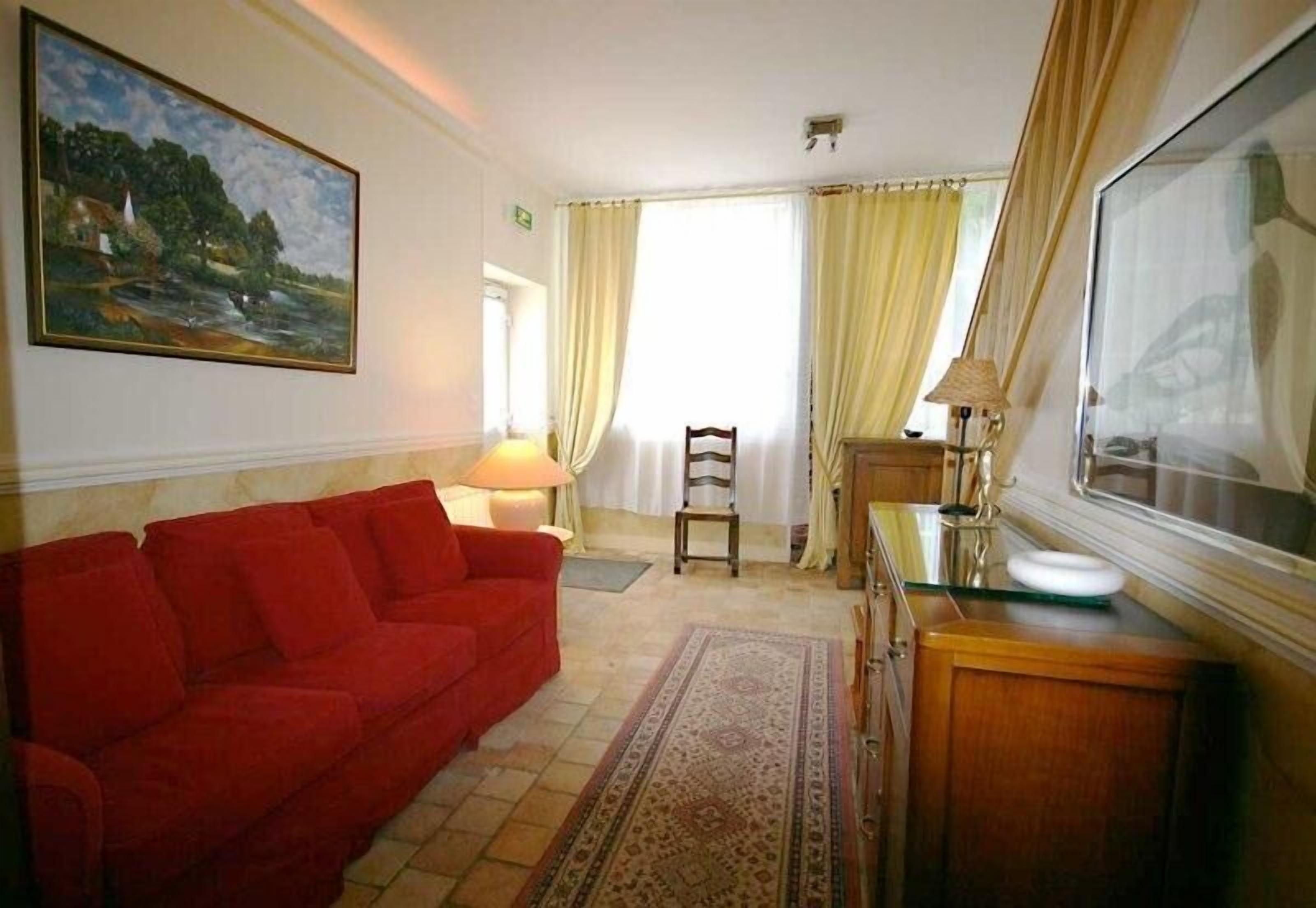 Una sala de estar con un sofá rojo, un aparador de madera, un cuadro en la pared y vista a un paisaje por la ventana.